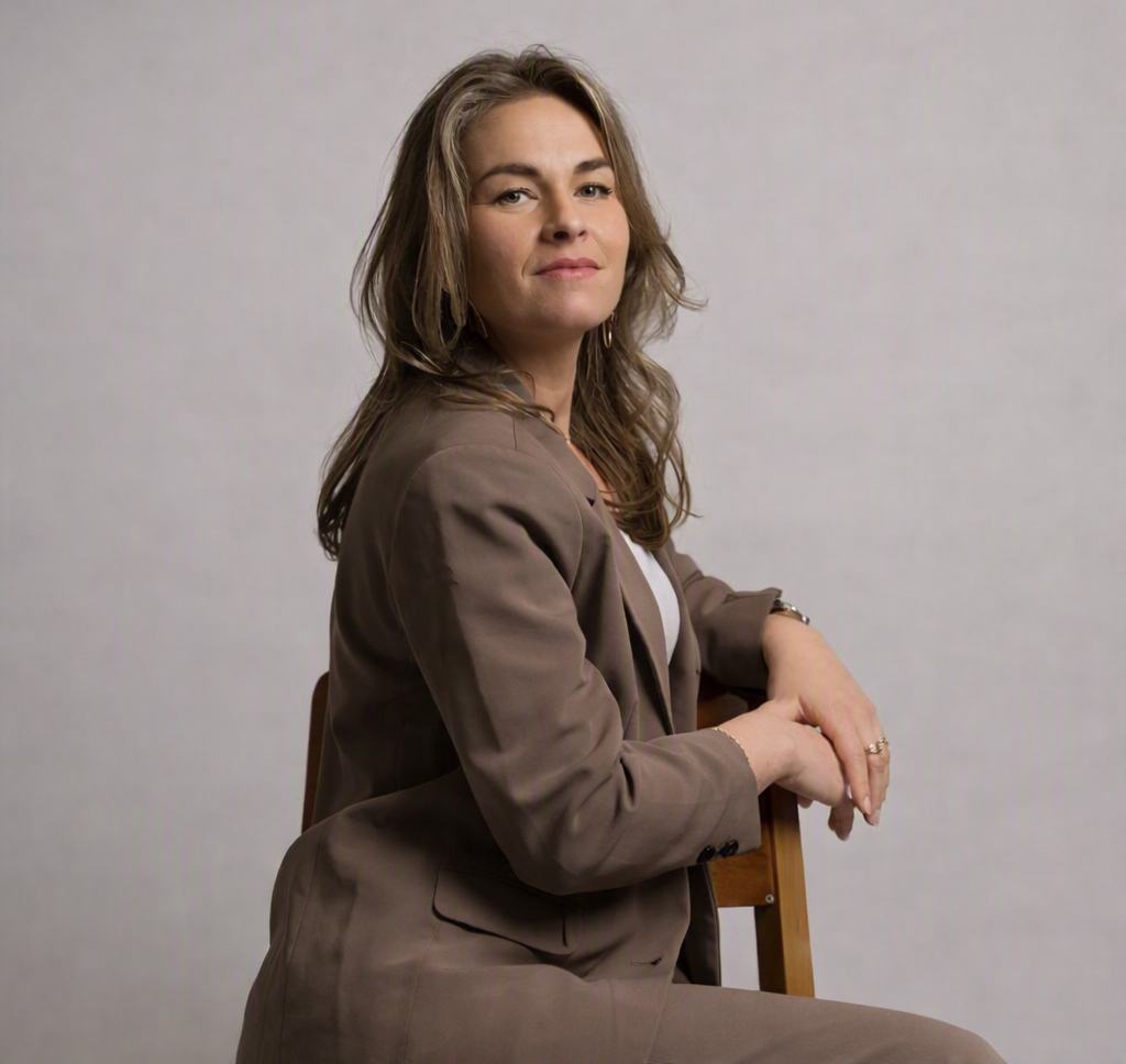 Katie Brouwer in een taupe blazer, zittend in haar praktijk